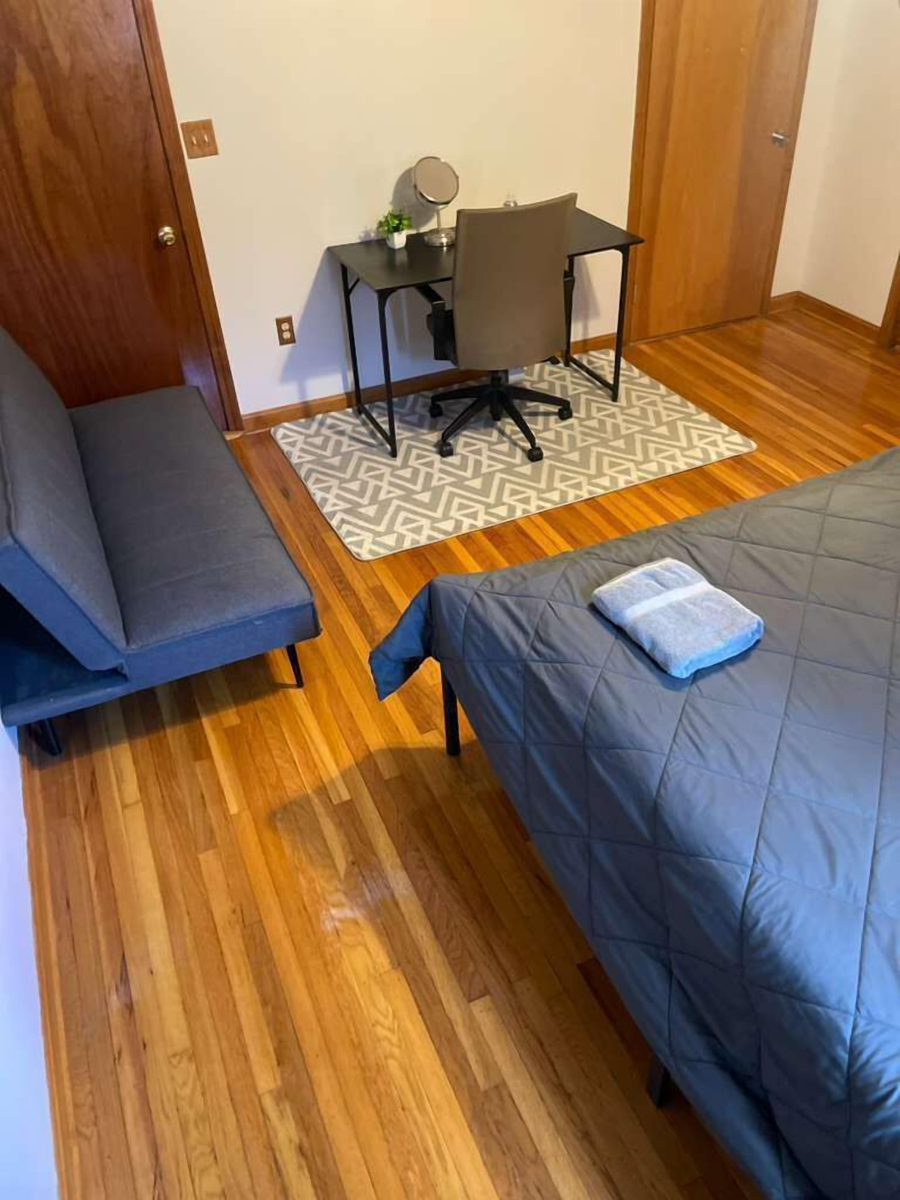 Une pièce de taille modeste comprenant un lit, un canapé, un petit bureau avec une chaise et un tapis à motifs.