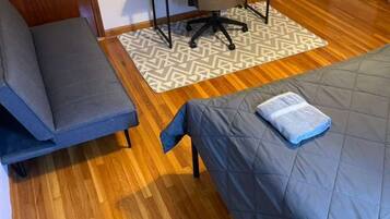 Une pièce de taille modeste comprenant un lit, un canapé, un petit bureau avec une chaise et un tapis à motifs.