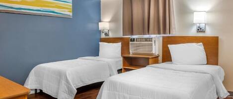 Quarto de hotel com duas camas de solteiro, uma mesinha de cabeceira de madeira, ar condicionado fixado na parede e um quadro na parede.