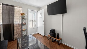Ein modernes Wohnzimmer mit einem an der Wand montierten Flachbildfernseher, einem Holzesstisch und einem kleinen Beistelltisch mit Lautsprechern.