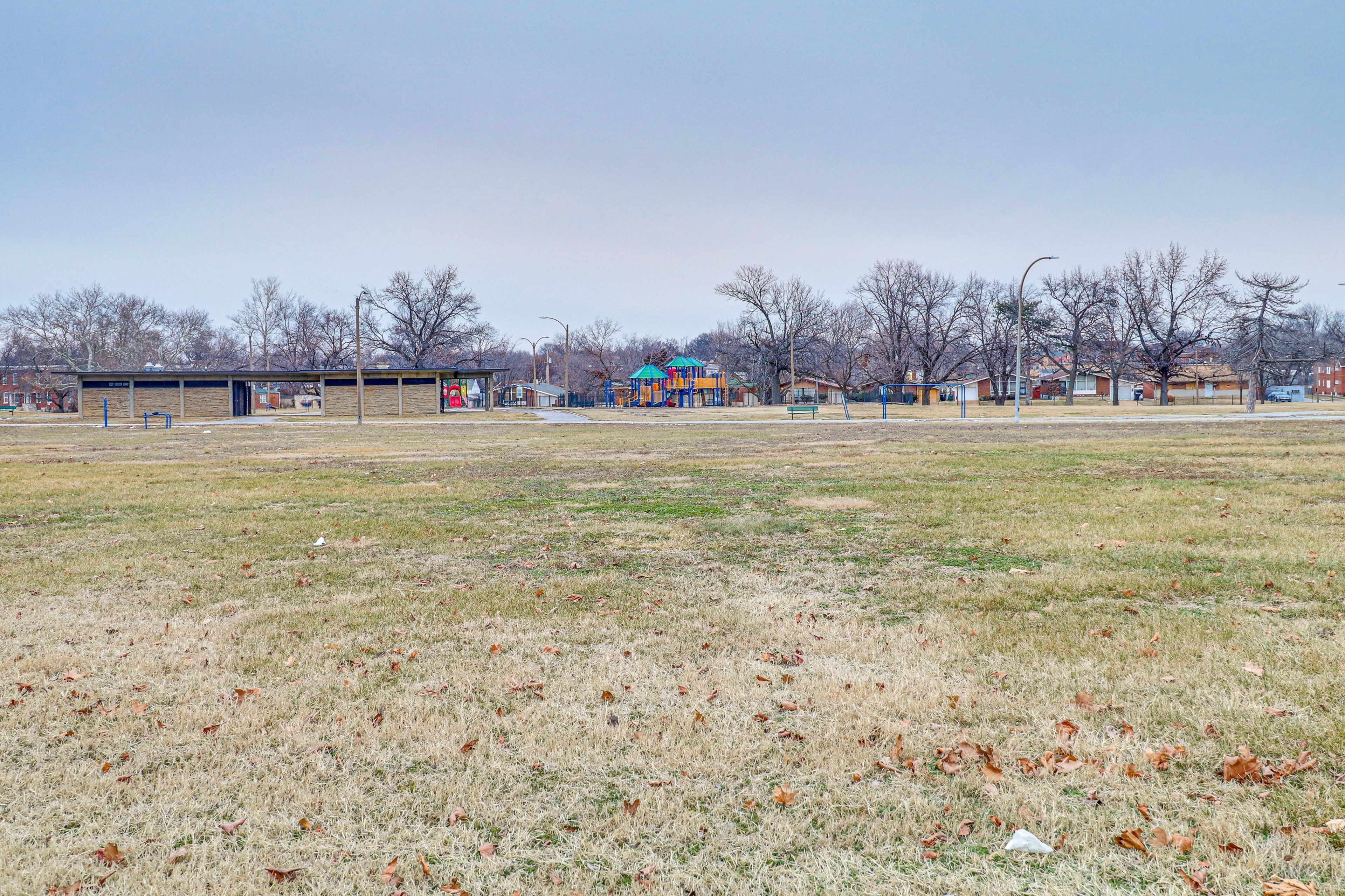 A playground with a blue and yellow structure, surrounded by a grassy field and leafless trees.