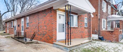A two-story brick house with a front porch, a garage, and a small front yard.