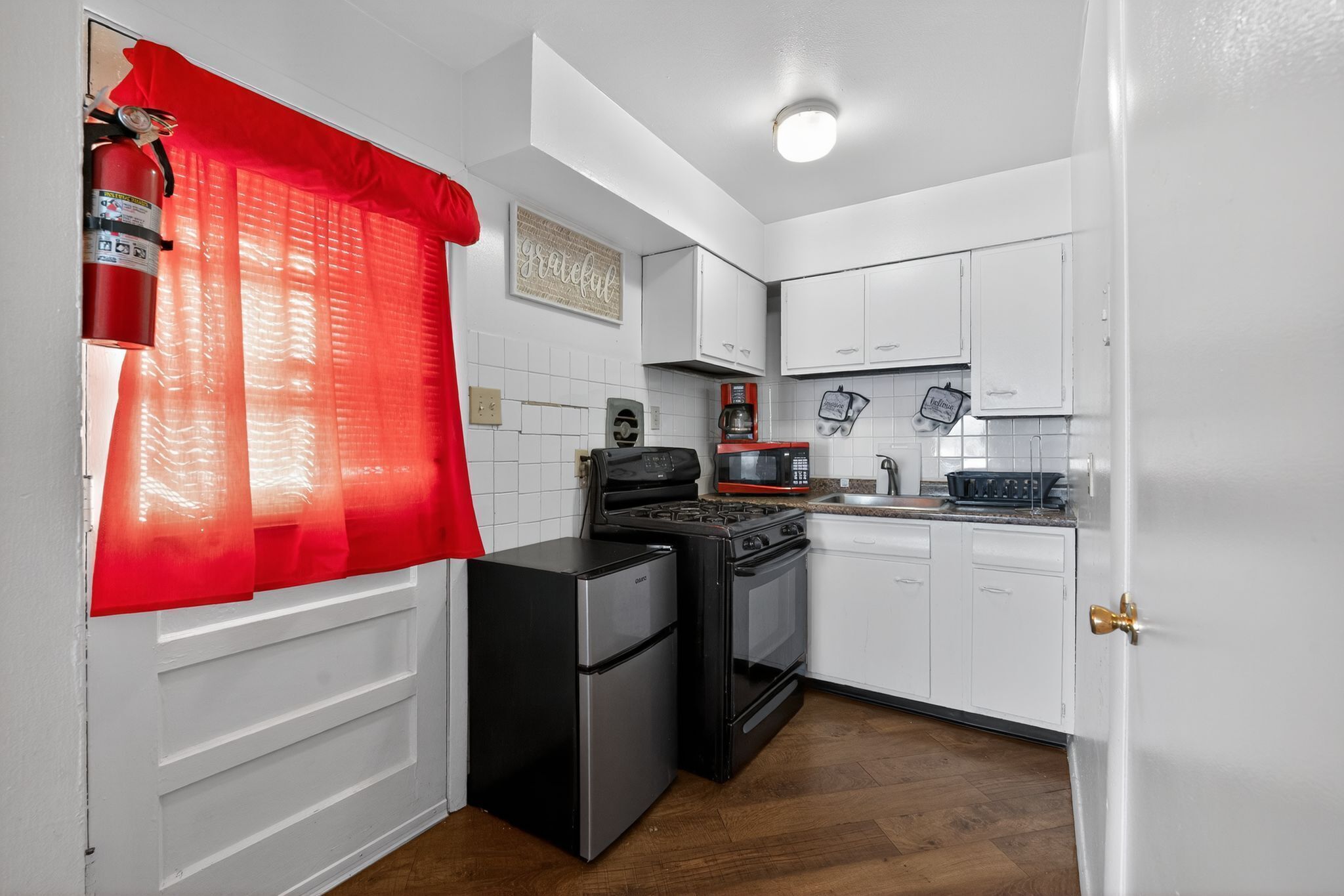 Una cocina compacta con armarios blancos, un refrigerador negro, una estufa y un microondas.