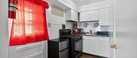 Una cocina compacta con armarios blancos, un refrigerador negro, una estufa y un microondas.