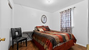 Ein Schlafzimmer mit einem Bett, einem Sessel, einem kleinen Tisch und einem Fenster mit gemusterten Vorhängen.