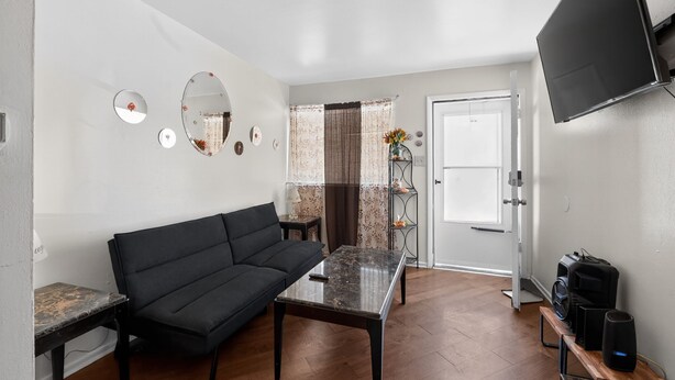 Ein modernes Wohnzimmer mit einer schwarzen Couch, einem Couchtisch mit Glastischplatte und einem an der Wand montierten Fernseher.