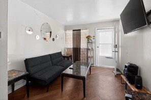 A modern living room with a black sofa, a glass-top coffee table, and a TV mounted on the wall. - Quaint St Louis Home ~ 6 Mi to Downtown! (St. Louis)