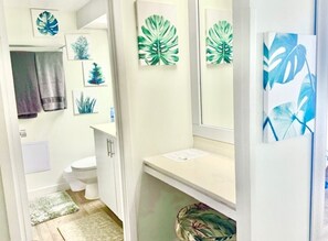 A bathroom with a toilet, sink, mirror, and wall-mounted artwork. - Stylish Studio- Stunning City View - Parking (Honolulu)