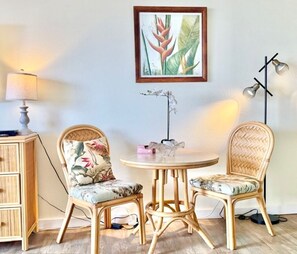 A room with two wicker chairs, a round table, a framed botanical print on the wall, a floor lamp, and a small side table with a lamp. - Stylish Studio- Stunning City View - Parking (Honolulu)