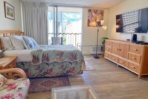A bedroom with a bed, wooden dresser, and a city view through the window. - Stylish Studio- Stunning City View - Parking (Honolulu)