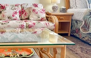 A room with a floral sofa, a glass-top coffee table, a wooden nightstand, and a patterned rug. - Stylish Studio- Stunning City View - Parking (Honolulu)