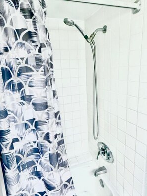 A shower with a handheld showerhead, a wall-mounted faucet, and a bathtub. - Stylish Studio- Stunning City View - Parking (Honolulu)