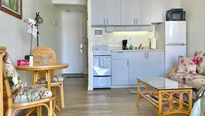Ett kompakt bostadsutrymme med ett litet kök, en matplats med ett runt bord och stolar samt en soffa med blommigt tyg.