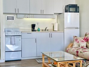 A compact kitchen with white cabinets, a microwave, a coffee maker, and a stove. - Stylish Studio- Stunning City View - Parking (Honolulu)
