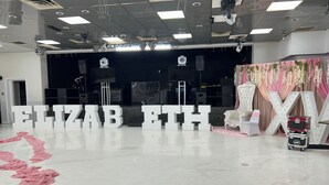 A spacious room with a polished floor, large white letters spelling "ELIZAB ETH," and a stage area with a pink floral backdrop. - Economy Inn of Reading (Reading)