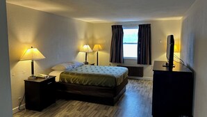A hotel room with a bed, bedside lamps, a desk with a computer, and a window with curtains. - Economy Inn of Reading (Reading)