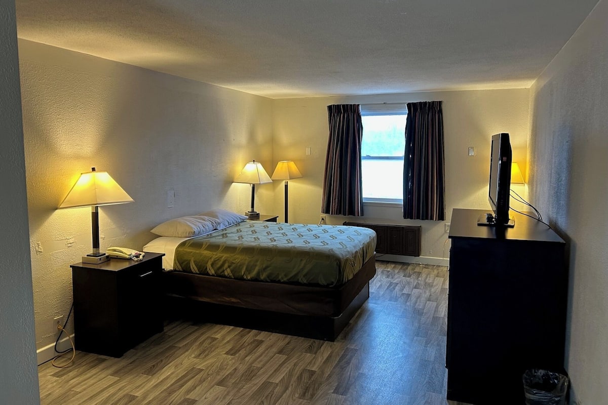 A hotel room with a bed, bedside lamps, a desk with a computer, and a window with curtains.