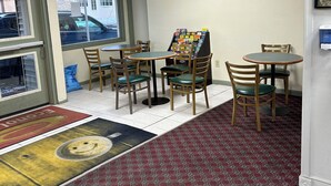 A restaurant interior with a tiled floor, wooden tables and chairs, a menu board, and a window with a view of the outside.