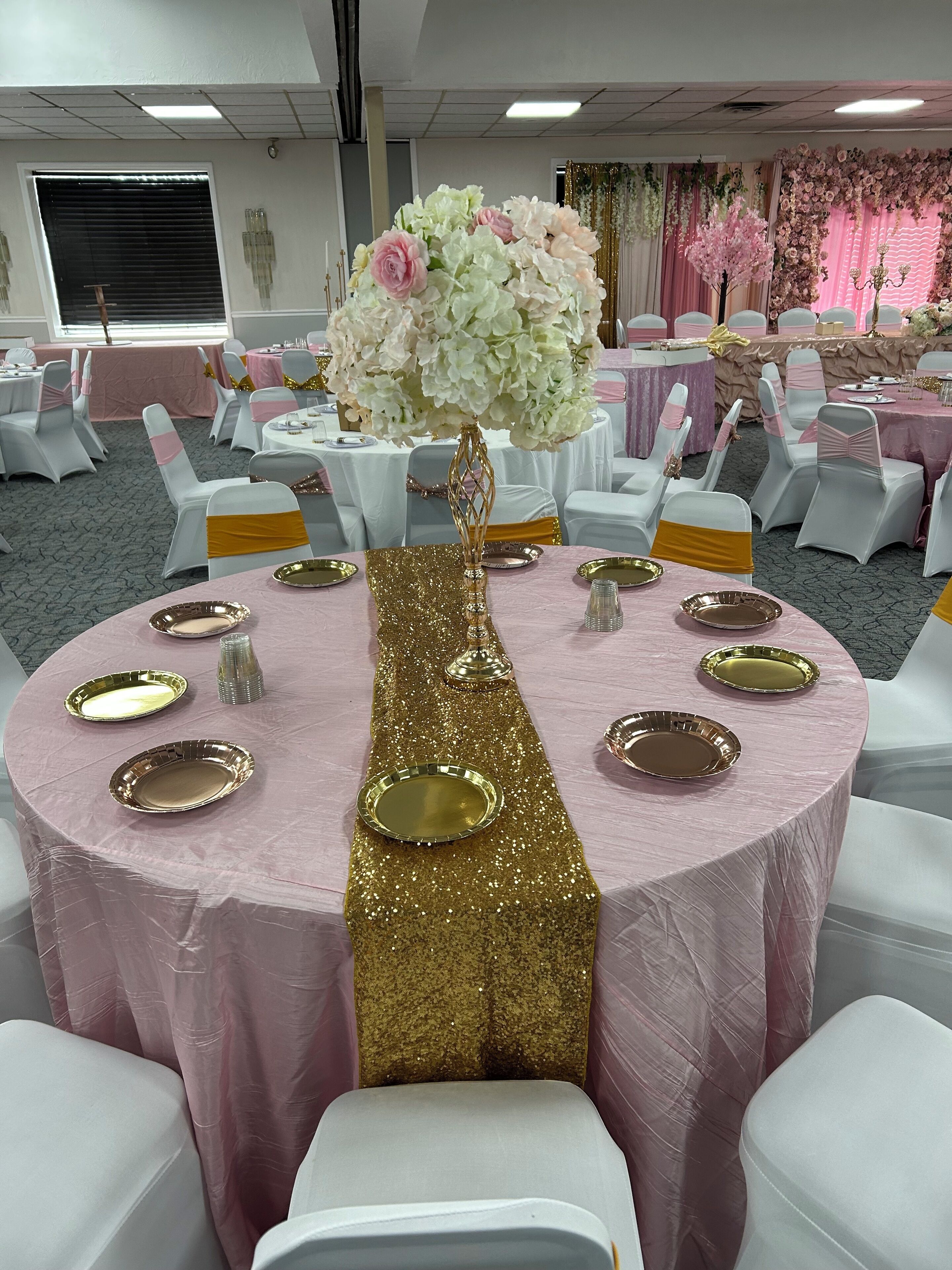 A banquet hall with round tables covered in pink tablecloths, gold sashes, and gold plates.