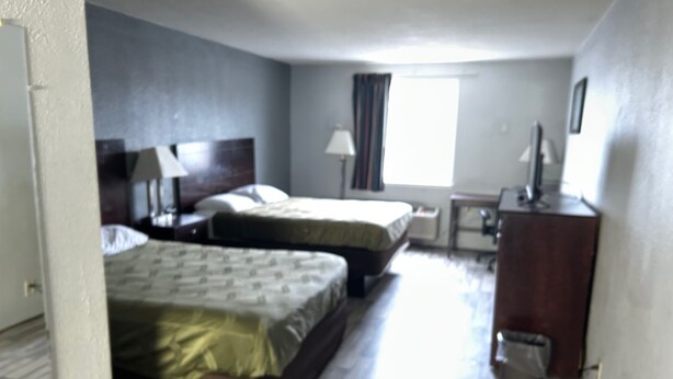 A hotel room with two beds, a desk, a chair, a lamp, and a window with curtains.