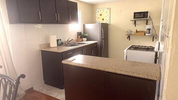 Cocina compacta con gabinetes oscuros, encimera de granito, refrigerador, microondas y cafetera.