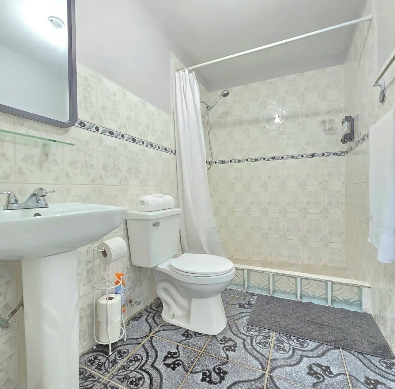A bathroom with a toilet, sink, shower, and patterned floor tiles.