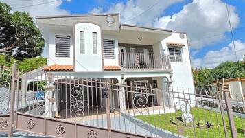 Una casa de dos pisos con balcón, entrada protegida por un portón y césped bien cuidado.