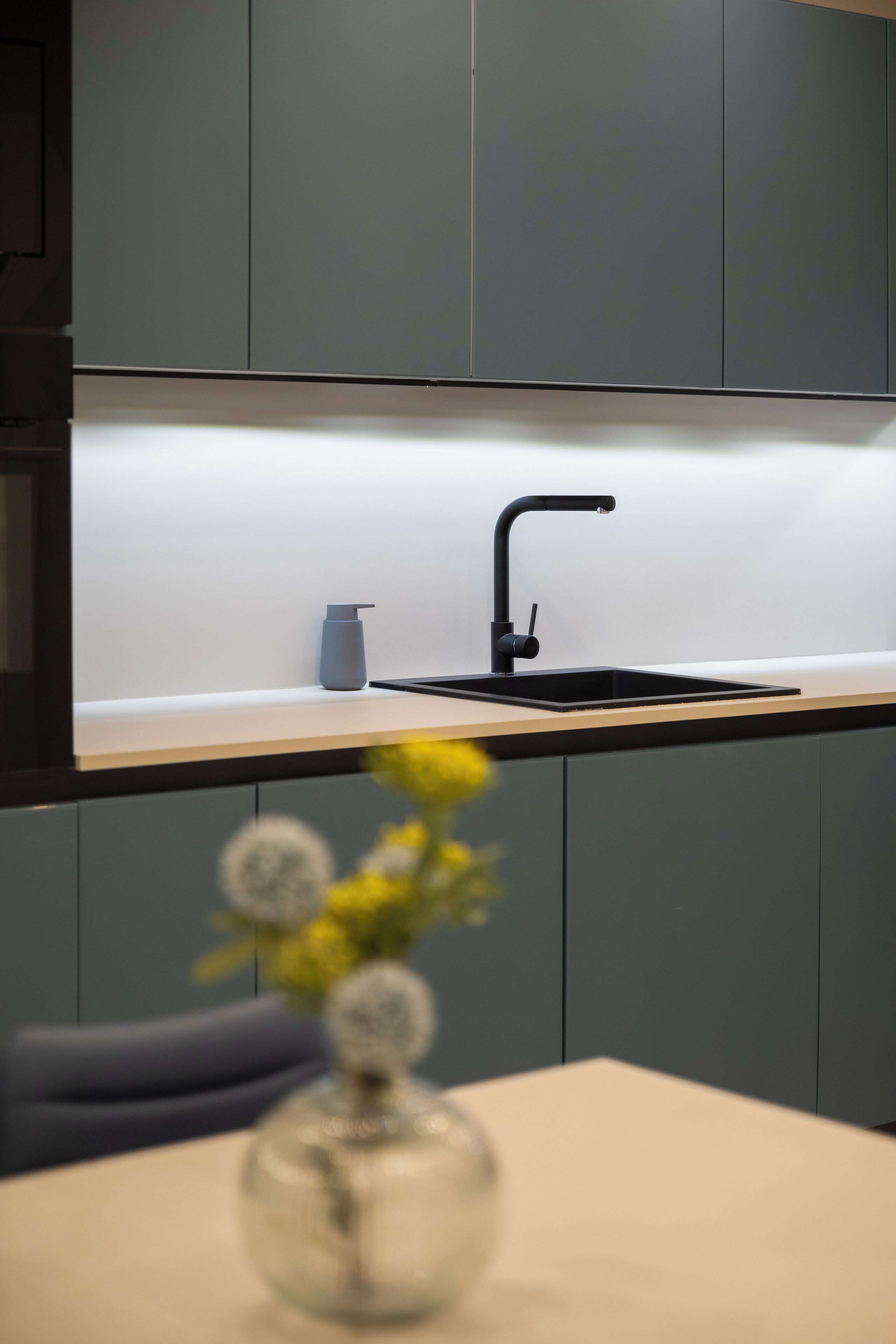 A modern kitchen with a black faucet, a small vase with flowers, and grey cabinets.