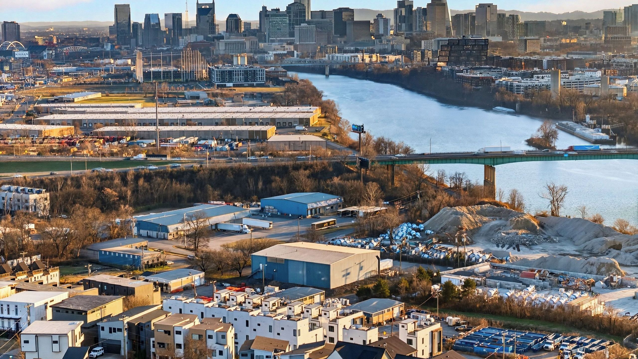 Une vue urbaine comprenant une rivière, des bâtiments industriels et un pont.