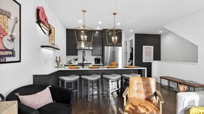 Una cocina moderna con una isla central, taburetes de bar y un comedor con sofá y sillas.