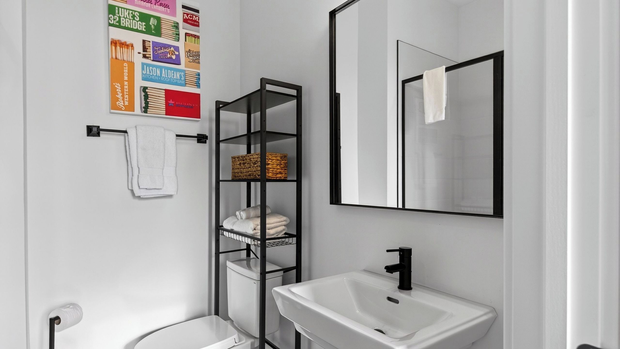 A modern bathroom with a white sink, a black metal shelf unit, and a large mirror.