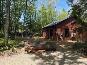 A red cabin with a gravel path leading to it, surrounded by trees.