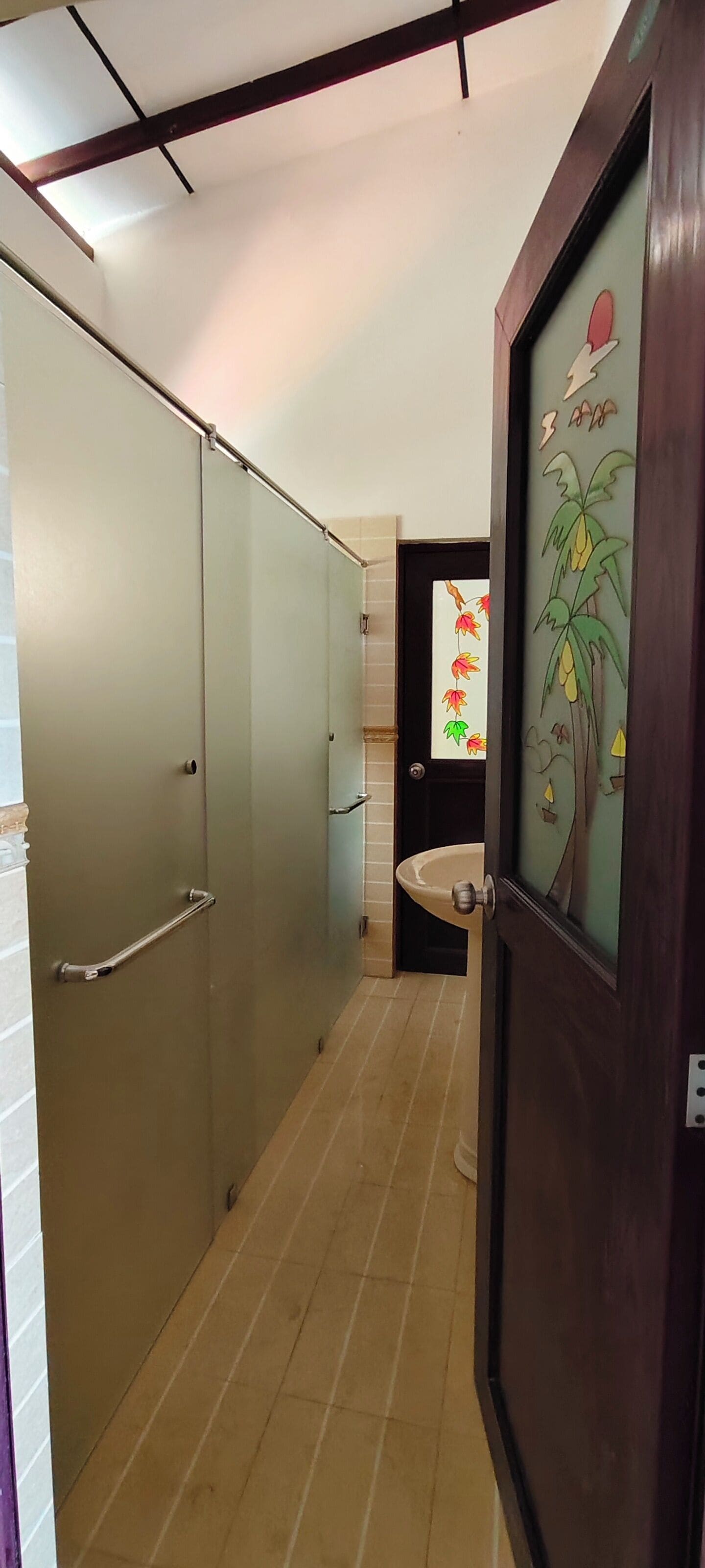 A narrow hallway with frosted glass doors, a wooden door with a decorative panel, and a sink with a glass enclosure.