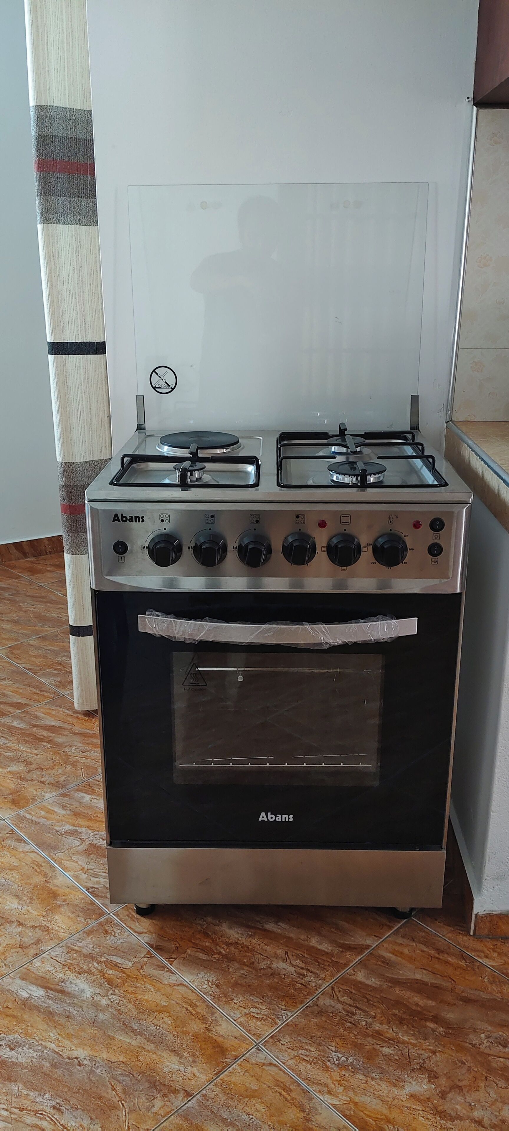 A stainless steel Abans gas stove with four burners and a built-in oven, located in a kitchen with tiled flooring.