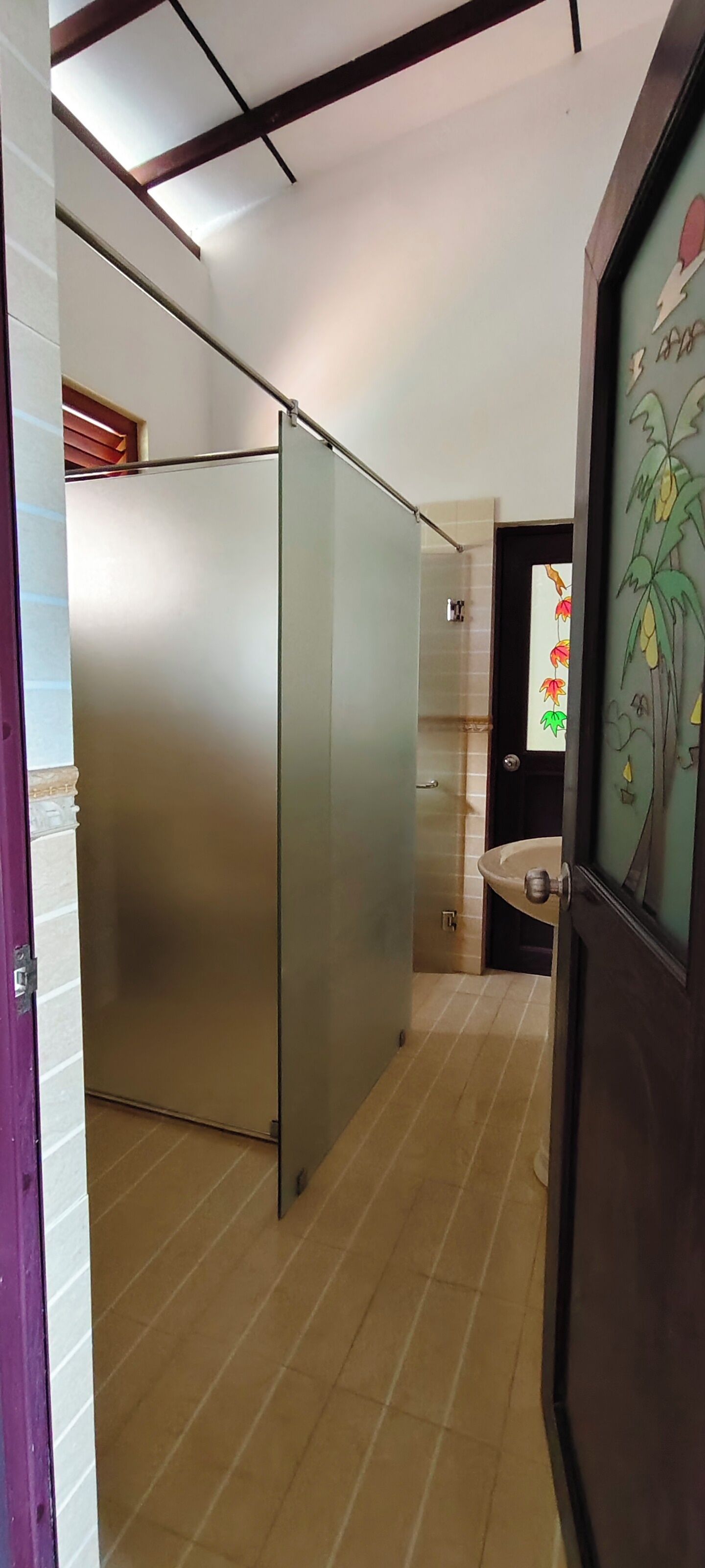 Un pasillo con una puerta corredera, suelo de baldosas y un baño con un lavabo e inodoro a la vista a través de la puerta.