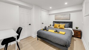 Ein modernes Schlafzimmer mit Bett, Nachttisch, Sessel und einer kleinen Pflanze.