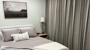 Ein Schlafzimmer mit Bett, Nachttisch, Lampe, einem Gemälde und Vorhängen.