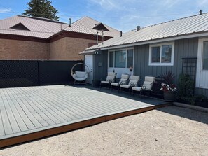 Un jardin avec une terrasse en bois, un espace de détente couvert avec des chaises, et une maison avec un toit en métal.