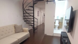 Ein Wohnzimmer mit Sofa, Treppe und einem an der Wand befestigten Fernseher.