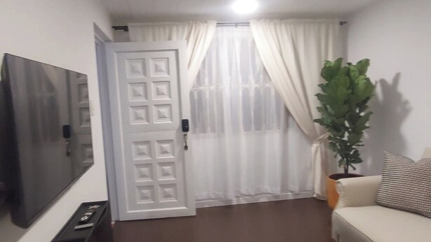 Ein Wohnzimmer mit Flachbildfernseher, einer Couch, einem Blumentopf und einer Tür mit Zahlenschloss.