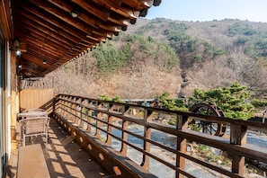 A wooden deck with a railing overlooking a forested area and a water wheel. - Gyeongju Palace Hanok Kids Pool Villa (Gyeongju)