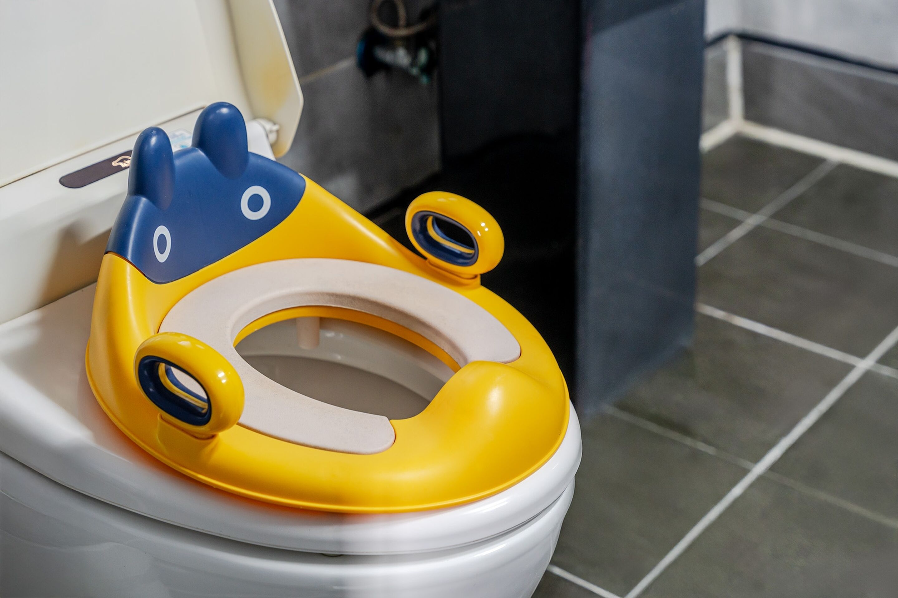 Un inodoro con un asiento infantil amarillo y azul.