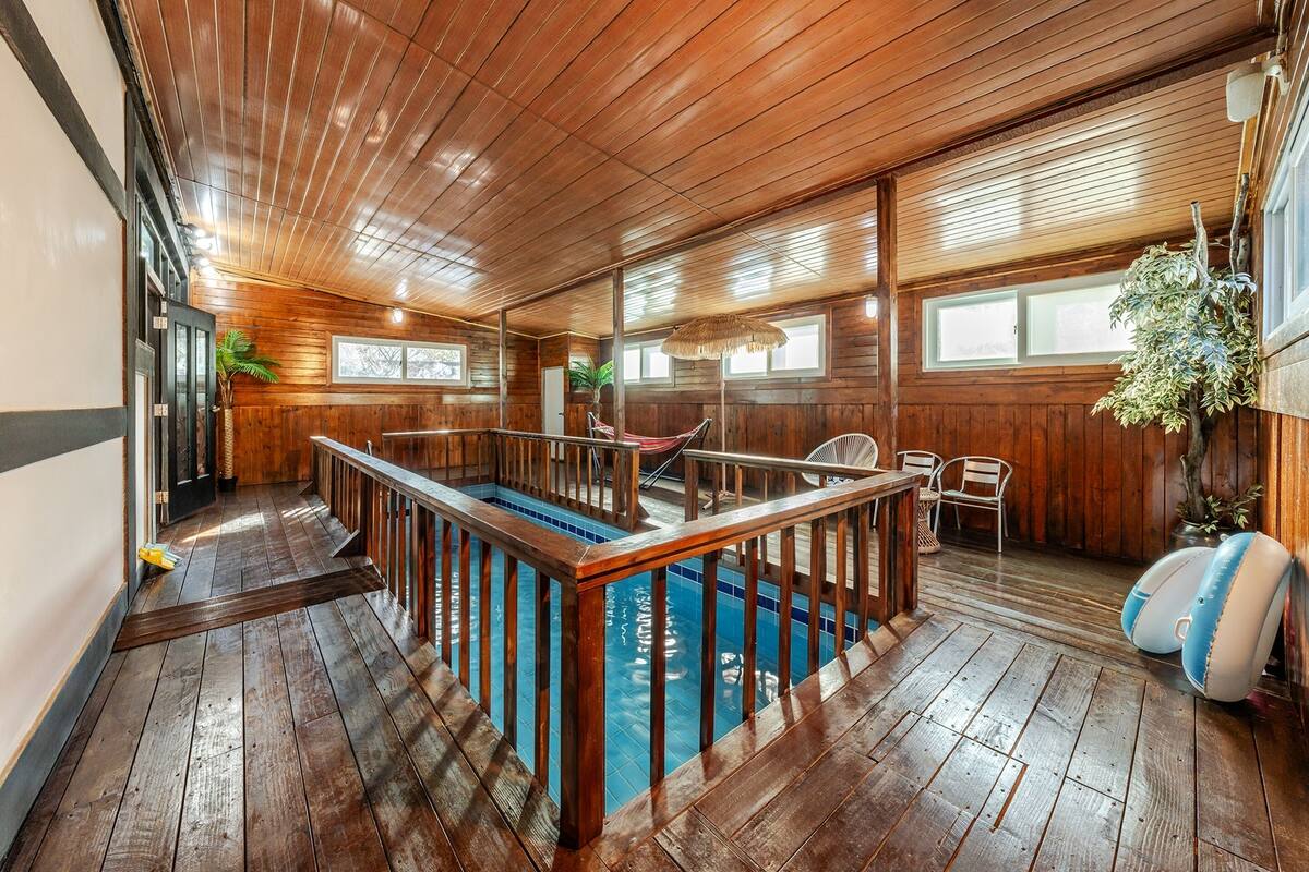 A wooden-floored room with a pool, a hammock, and a dining area.
