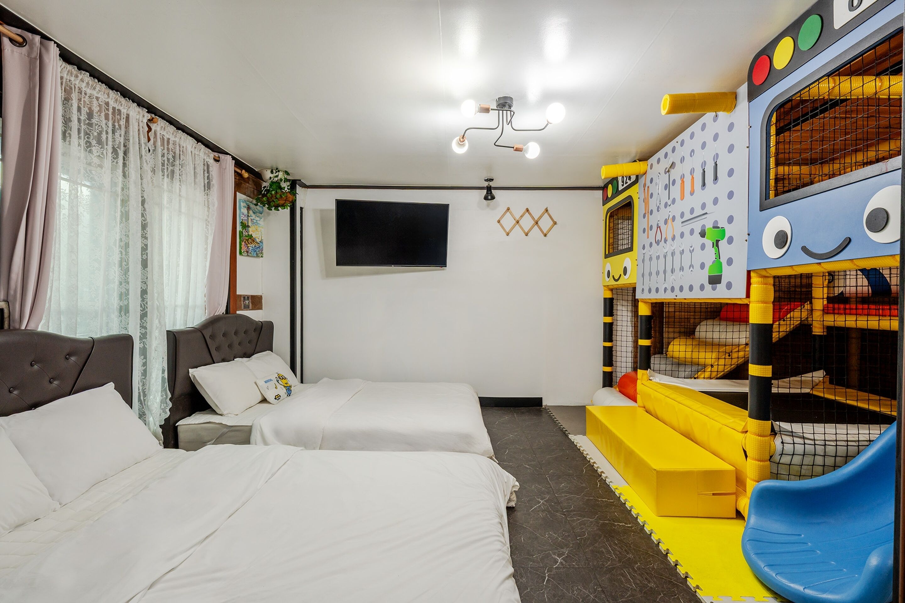 Une chambre d’hôtel avec deux lits, une télévision, un espace de jeux avec un toboggan et un luminaire au plafond.