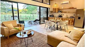 Una sala de estar moderna con sofá, mesa de centro y comedor. Una ventana grande ofrece vistas al exterior.