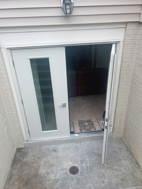 Une porte-fenêtre coulissante donnant sur un espace extérieur abrité, doté d’un sol en béton et d’un paillasson.