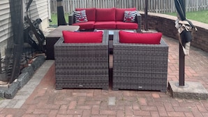 A covered patio area with wicker furniture and red cushions. - 3-bedroom apartment in Woodbridge close to shopping centers, Quantico and DC. (Woodbridge)