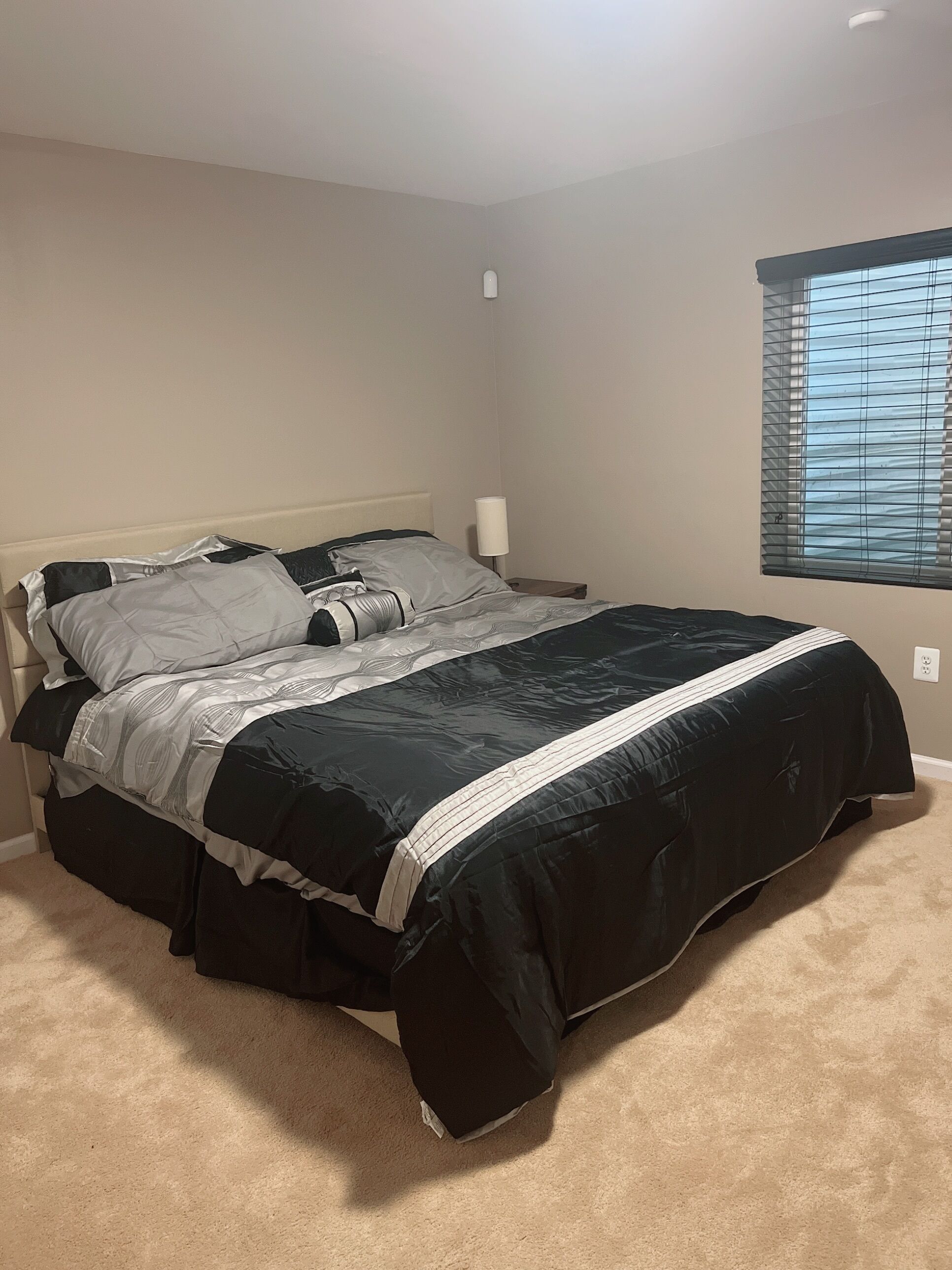 Une chambre à coucher avec un lit, une table de chevet, une lampe et une fenêtre avec des stores.