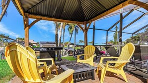 Eine Terrasse im Freien mit gelben Adirondack-Stühlen, einem Grill und einer Glaskonstruktion.