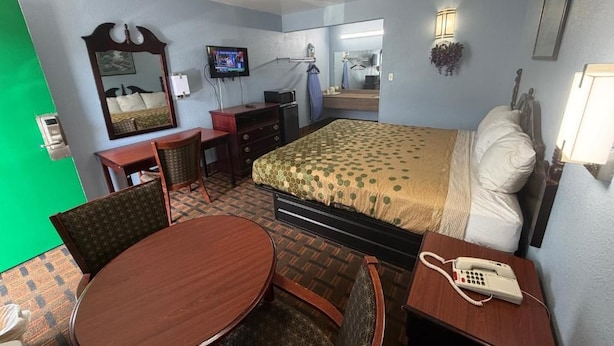 A hotel room with a bed, a desk with a telephone, a chair, a table, and a television. - TRAVEL INN (Richmond)